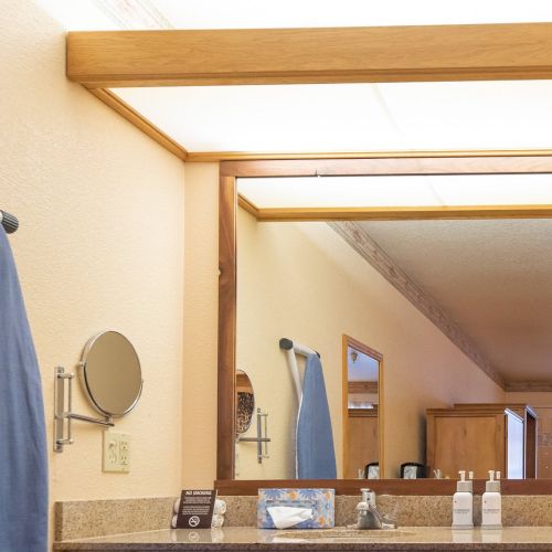 A bathroom mirror reflects an ironing board, wall-mounted mirror, tissue box, soap dispensers, and towels on a granite countertop.