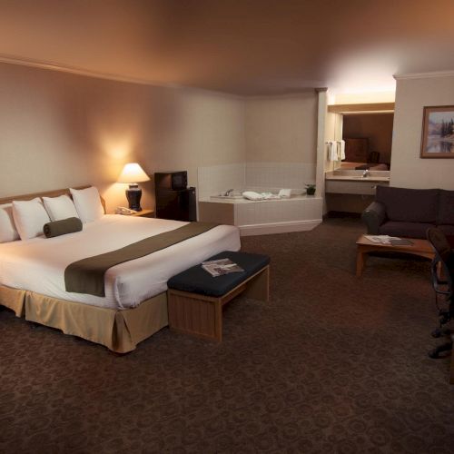 A hotel room with a bed, lamps, jacuzzi, sofa, desk with a laptop, and decor on the walls, creating a cozy atmosphere.