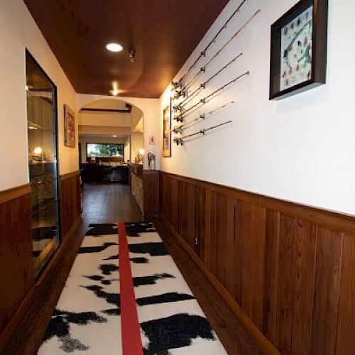 A hallway with wooden paneling, a cow-patterned rug with a red stripe, fishing rods displayed on the wall, and a framed artwork ending the sentence.