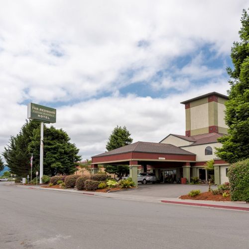 A hotel building with a red roof, surrounding greenery, a signpost, and a cloudy sky in the background.