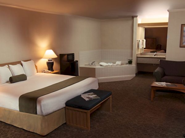 A hotel room with a king-sized bed, nightstands with lamps, a jacuzzi, a seating area, a desk with a laptop, and a TV.