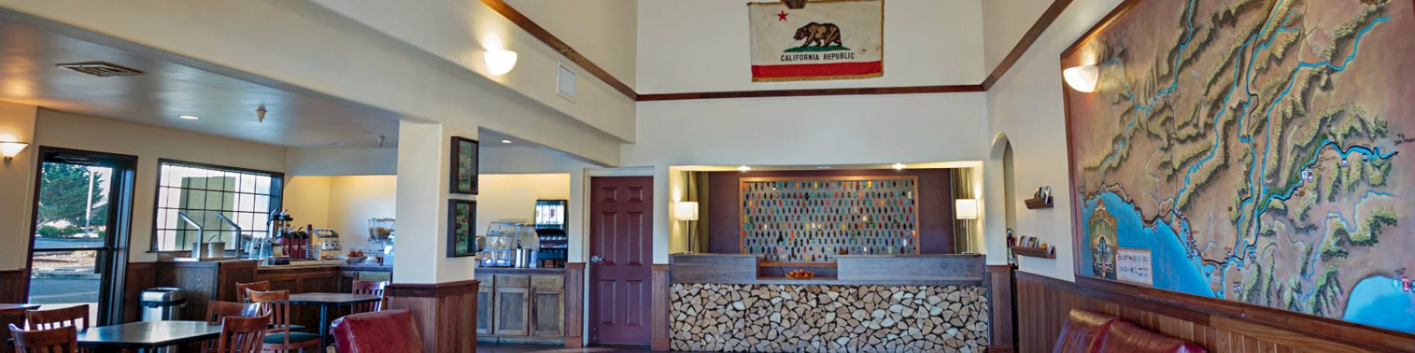 This image shows a lobby area with red chairs, a front desk, a map on the wall, and a seating area with tables and chairs on the side for dining.