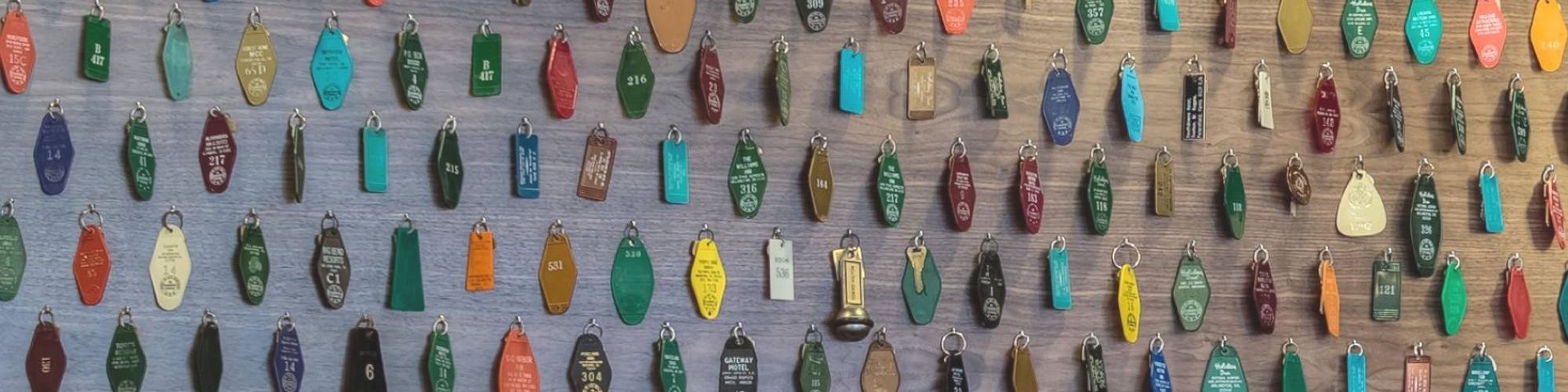 The image shows a wall covered with an assortment of colorful vintage hotel key tags and key holders.