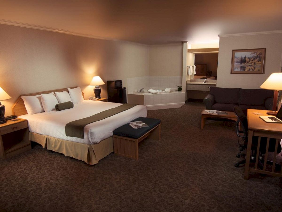 This image shows a spacious hotel room with a king-sized bed, a sofa, a desk, a whirlpool bathtub, two lamps, and a TV, creating a cozy atmosphere.