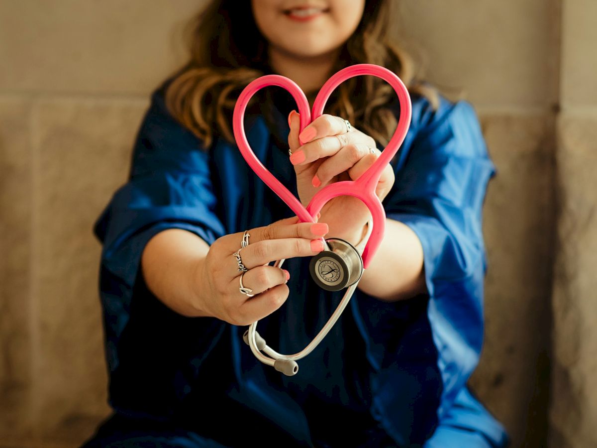A person in blue holds a stethoscope bent into a heart shape, highlighting healthcare and compassion.
