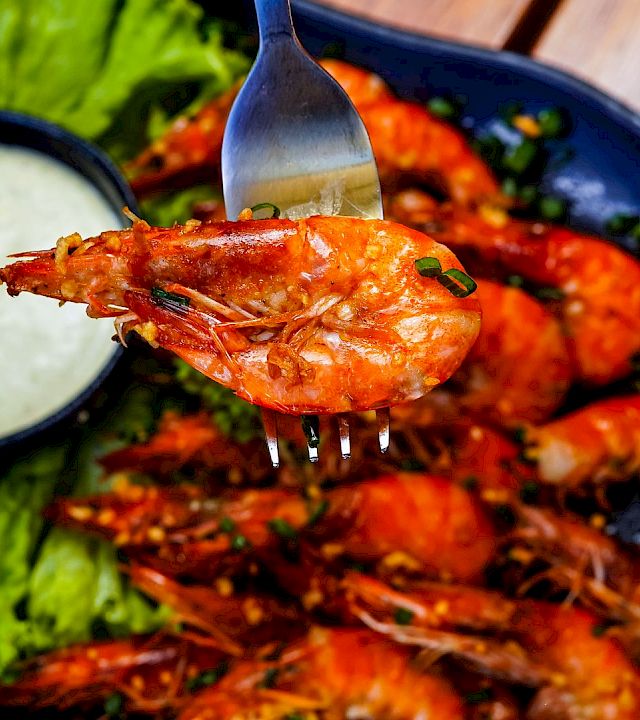 Juicy grilled shrimp with a tangy dipping sauce, fresh lettuce, lime wedges, and a vibrant plate of seafood on a rustic table.