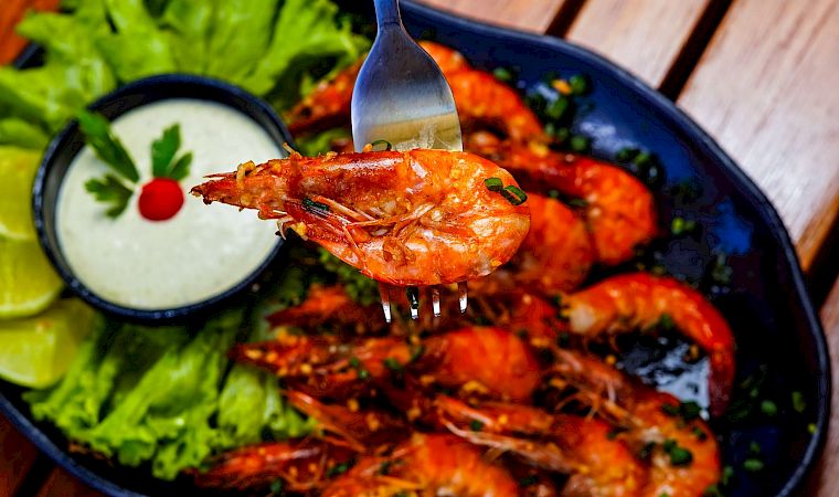 Juicy grilled shrimp with a tangy dipping sauce, fresh lettuce, lime wedges, and a vibrant plate of seafood on a rustic table.